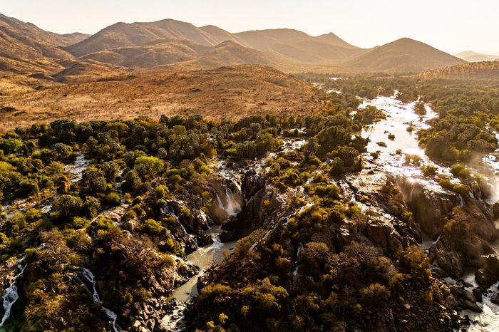 Luftaufnahme der Epupa-Wasserfälle am Kunene mit grüner Vegetation und Bergen